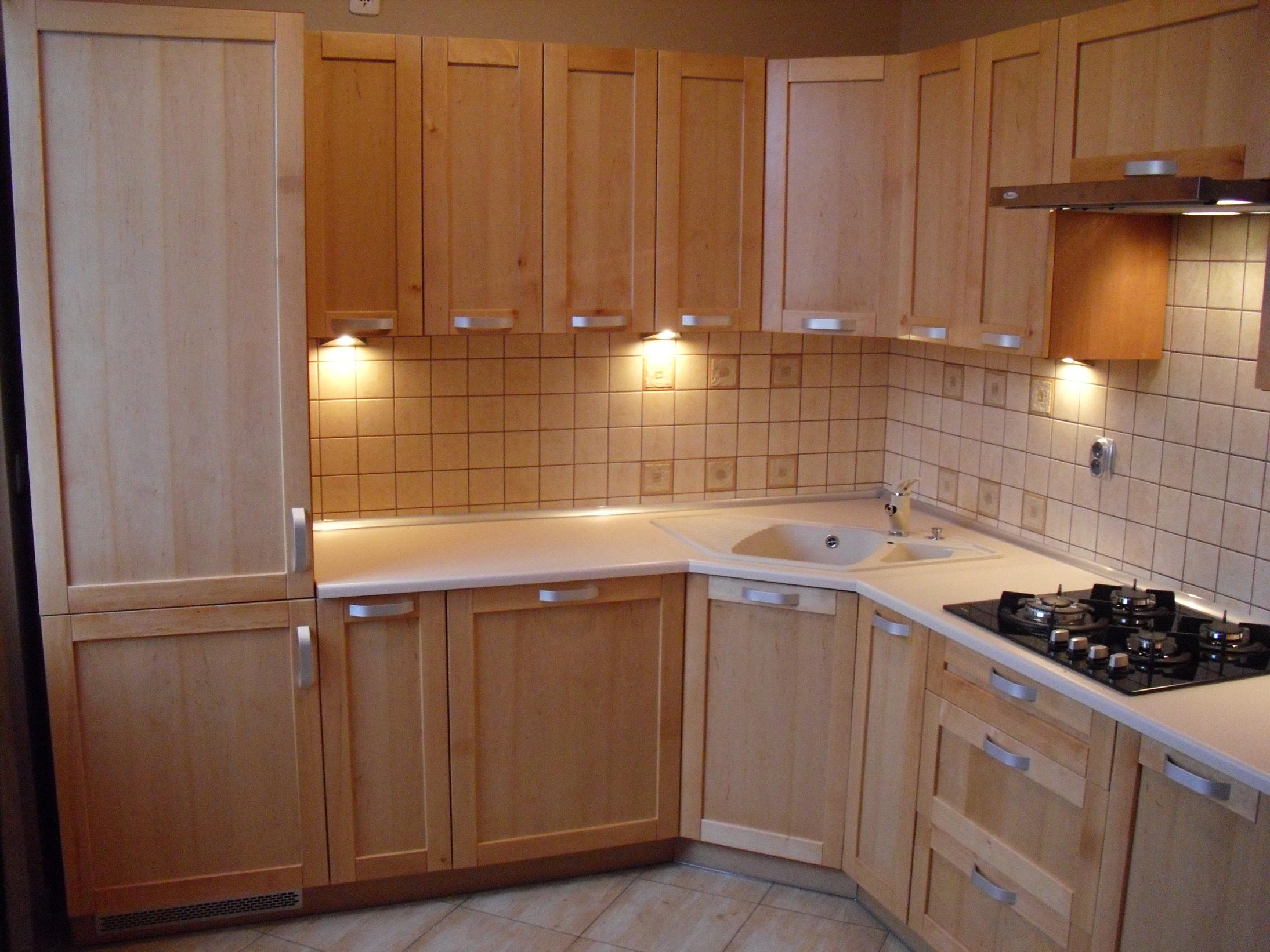 Jasna kuchnia na wymiar z drewnianymi frontami, ceramiczną płytą grzewczą i beżowymi kaflami na ścianie, oświetlona punktowymi lampkami podszafkowymi.